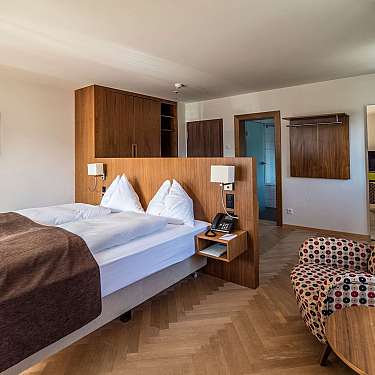 Modernes Hotelzimmer mit Doppelbett, Holzverkleidung, Sessel mit Muster und Fenster mit Vorhängen, content_suitable:true