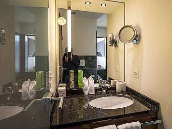 Modern bathroom vanity with oval sink, large mirror, chrome fixtures, towels, and toiletries on a dark countertop