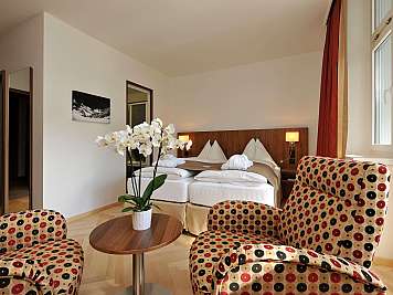 Bright hotel room with twin beds, patterned armchairs, and a potted orchid by the window.