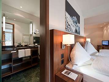 Bright hotel room with bed, mountain artwork, and adjacent bathroom vanity area