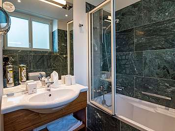 A modern bathroom with dark green tiled shower walls, a white sink, and a bathtub with glass screen