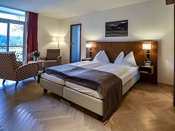 A tidy hotel room with a double bed, armchairs by a window, and mountain views outside. 
