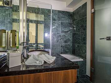 Modernes Badezimmer mit dunklen Steinfliesen, Glasdusche, Waschbecken und Handtuch auf der Ablage, content_suitable: true