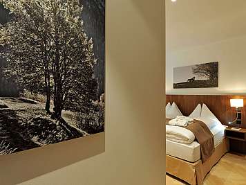 Modernes Hotelzimmer mit frisch gemachtem Bett, Nachttischlampe und Landschaftsbildern an der Wand, true