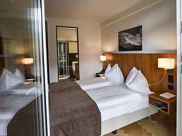 Neatly made hotel room with twin beds, wood headboard, bedside lamps, and a mountain wall print.