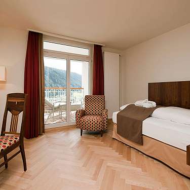 Spacious hotel room with bed, patterned chairs, desk, and balcony view of mountains,content_suitable=true}