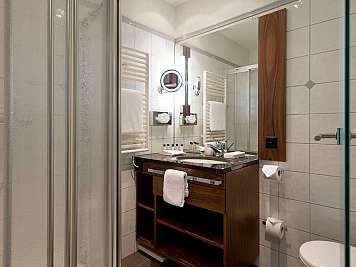 Bright tiled bathroom with glass shower, wooden vanity, large mirror, and white towels.,