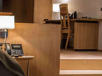 Warm wood-paneled hotel room with desk lamps, a telephone, and a chair at the back wall.