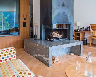 Moderner Wohnraum mit zentralem Kamin, Holzverkleidung, Schreibtisch und gepunkteter Polsterbank in warmen Holztönen. Zum Inhalt