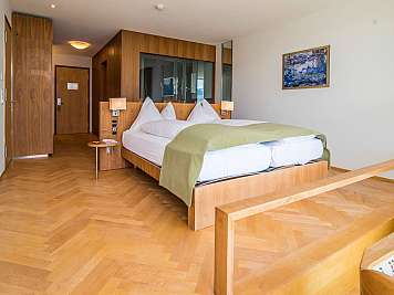 Modern hotel bedroom with a wooden bed, white bedding, and green throw blanket, plus a chair and wall art
