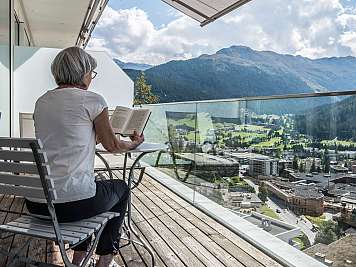 Ältere Frau liest auf einem Balkon mit Berg- und Talblick im Hintergrund, content_suitable=true