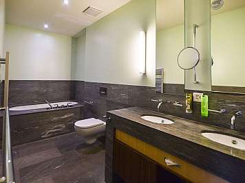 Modern bathroom with double sink vanity, bathtub, toilet, and large wall mirror in dark stone finishes, content_suitable:true