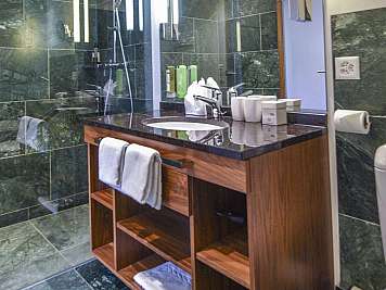 Modernes Badezimmer mit dunklen Steinfliesen, großer Dusche, Holzwaschtisch und beleuchtetem Spiegel, content_suitable:true}