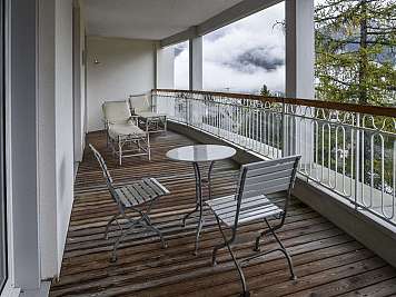 Wooden balcony with metal chairs and a small table overlooking misty mountains and trees