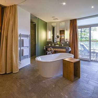 Modern bathroom with freestanding tub, double vanity, robe closet, and balcony doors open to outdoor seating.