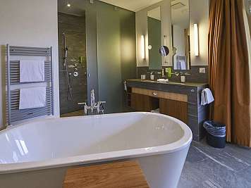 Modern bathroom with freestanding tub, double vanity, shower, and large mirrors by a window.