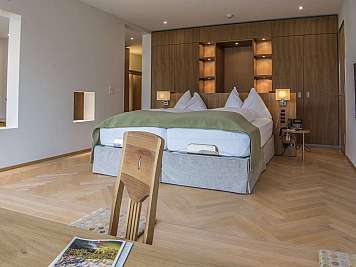 Modernes Hotelzimmer mit großem Doppelbett, Holzverkleidung, Nachttischlampen und hellem Parkettboden, content_suitable:true