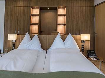 Modernes Hotelzimmer mit zwei Einzelbetten, Holzverkleidung, Nachttischlampen und Telefonen am Bettende.