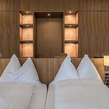 Modernes Hotelzimmer mit zwei Einzelbetten, Holzverkleidung, eingebauten Regalen und zwei Nachttischlampen, warm beleuchtet, content_suitable true