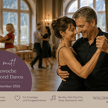 A smiling couple dances closely in a ballroom with other dancers in the background.