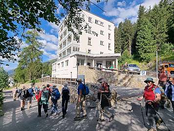 Group of hikers walking past a white mountain hotel on a forest road