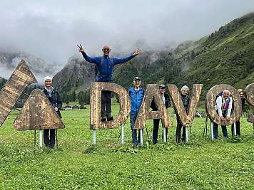 Group of hikers posing with large wooden DAVOS letters in a misty mountain valley.