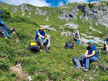 Group of hikers resting on a grassy mountain slope with rocky cliffs.