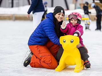 Woman and child pose on the ice with a yellow skating aid.