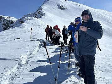 A group of hikers stands on a snowy mountain ridge with trekking poles.