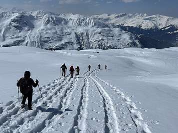 Group of hikers with poles walking across snowy mountain terrain.