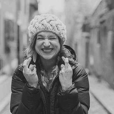 Lachende Frau mit Mütze und Winterjacke in einer schmalen Gasse