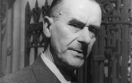 Close-up of a serious man in a suit standing by an ornate iron gate, black and white portrait imagery. 