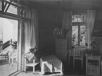 A black-and-white bedroom with open French doors, a bed, desks, chairs, and curtains by bright windows,content_suitable":true