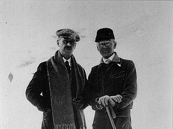 Two men in winter clothing stand on skis