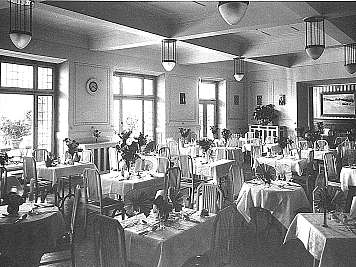A bright dining hall with many set tables, striped chairs, large windows, and hanging ceiling lights, content_suitable:true