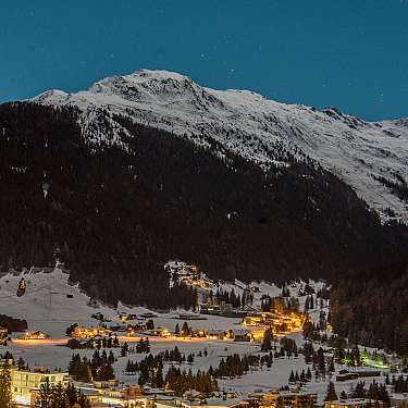 Beleuchtetes Dorf in einem verschneiten Tal unter einem großen Berg