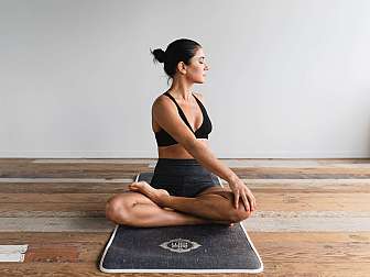 Woman sitting on yoga mat doing a twist in cross-legged position