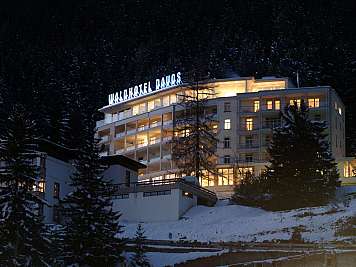 Lit hotel building at night surrounded by snow and tall pine trees