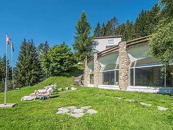 Grassy hotel lawn with sun loungers, flags, and a stone-and-glass building