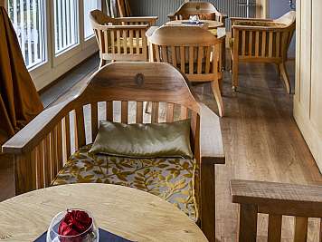 Wooden chairs and tables in a bright lounge with large windows and curtains.