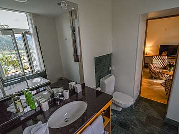 A modern bathroom with a sink, toilet, bathtub, and open view to a mountain landscape.