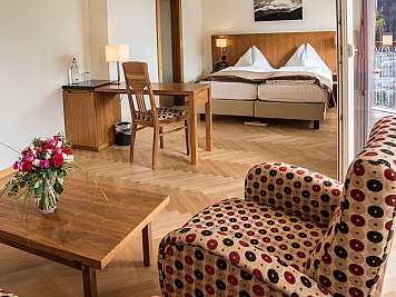Helles Hotelzimmer mit Bett, Schreibtisch, Stuhl, Sofa und Blumen auf dem Tisch.