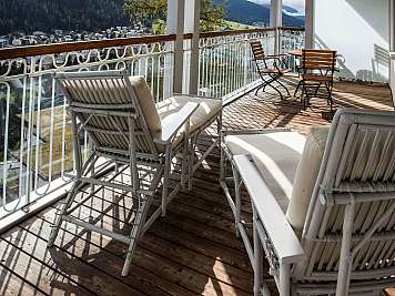 Terrasse mit weißen und hölzernen Sitzmöbeln und Blick auf ein Bergdorf