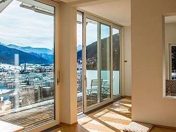 Helles Wohnzimmer mit großen Glasfronten und Blick auf verschneite Berge.