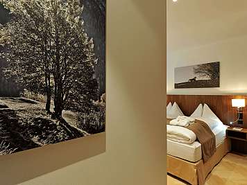 Warm hotel bedroom with a neatly made bed, wall lamp, and landscape photos.