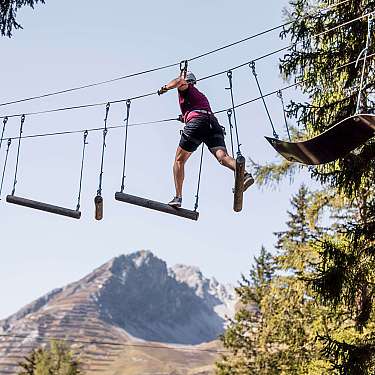 Person wearing a helmet crossing suspended logs on a forest ropes course.