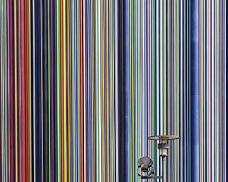 Vertical multicolored stripes cover a tall building exterior with a small sign and light fixtures.