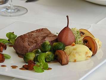 Gepökeltes Rindfleisch mit Kartoffelpüree, Gemüse und einer Birne auf weißem Teller.