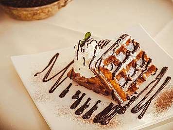 Blätterteigdessert mit Puderzucker, Schokoladensoße und einer Kugel Sahne auf einem Teller