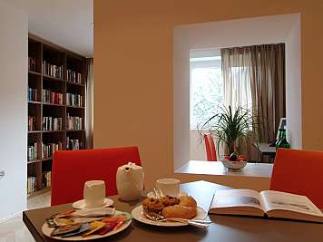 Dining table with pastries, cups, and an open book in a modern room with bookshelves